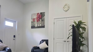 Ein modernes Wohnzimmer mit einem schwarzen Ledersofa, einem Relaxsessel, einem Flachbildfernseher auf einem Beistelltisch und einer Topfpflanze.