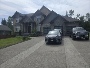 A large stone house with a driveway, two parked cars, and a garage.