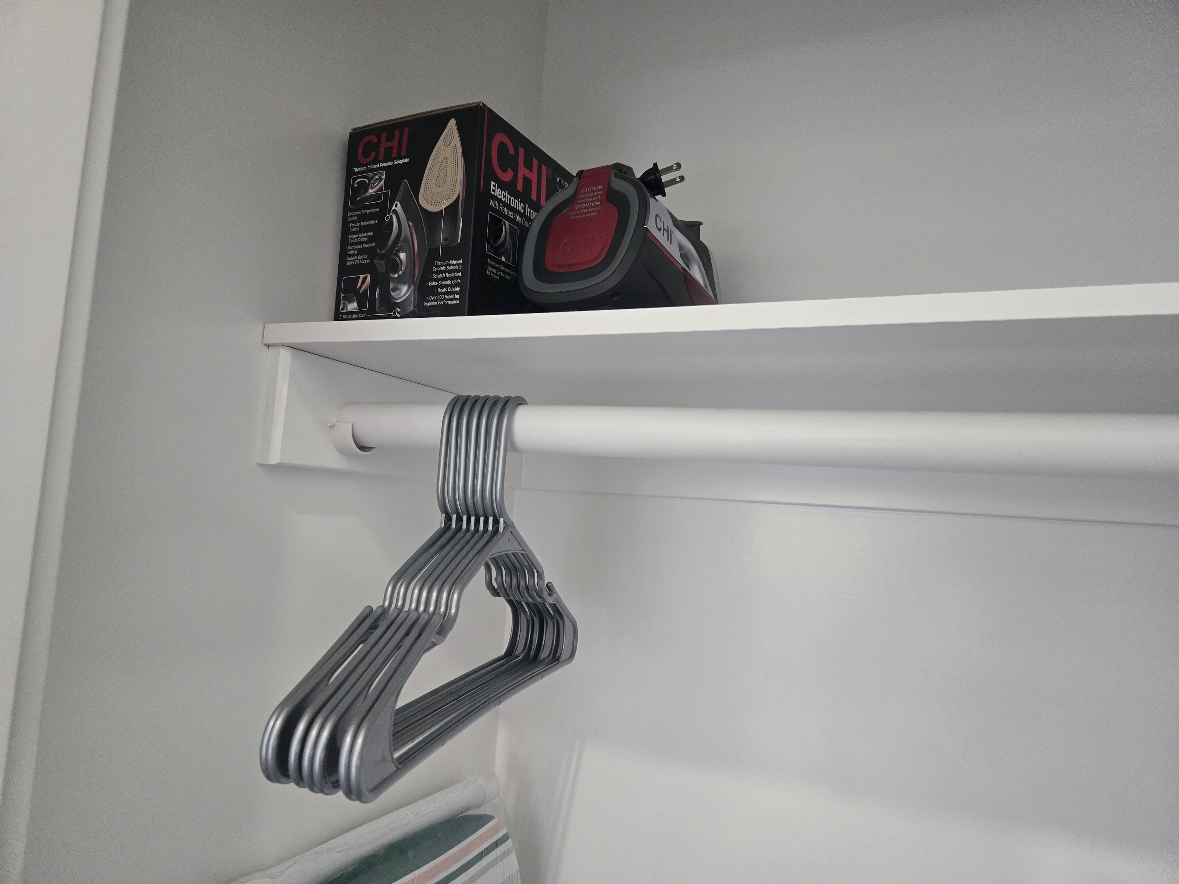 A white wall with a shelf holding a box labeled "CHI" and a red and black iron.
