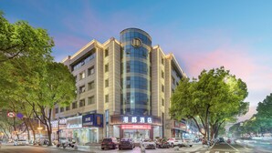 A modern hotel with a prominent curved glass facade, multiple floors, and a visible entrance with signage. - gangduhotel (Shaoxing)