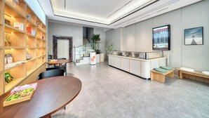 A modern reception area with a wooden reception desk, a seating area with cushioned benches, and a bookshelf filled with books and decorative items. - gangduhotel (Shaoxing)