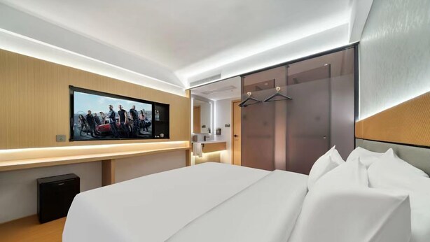 A modern hotel room with a large bed, a flat-screen TV mounted on the wall, a walk-in closet, and a sliding door closet. - gangduhotel (Shaoxing)