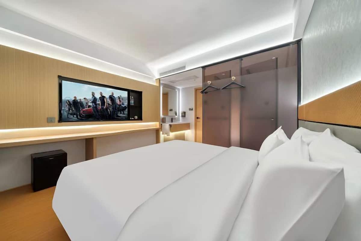 A modern hotel room with a large bed, a flat-screen TV mounted on the wall, a walk-in closet, and a sliding door closet.