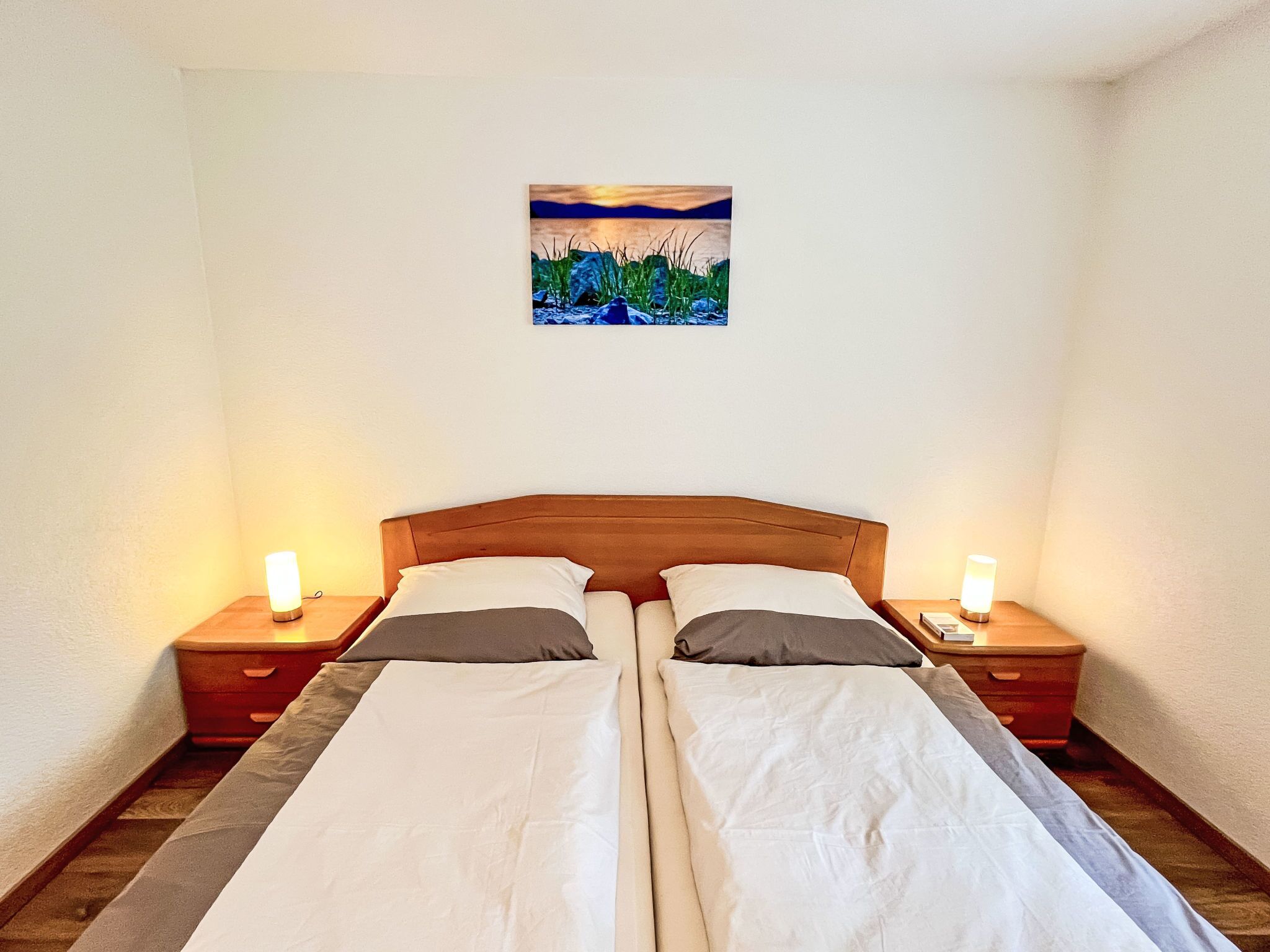 A double bed with two nightstands, each with a lamp, in a room with a painting on the wall.
