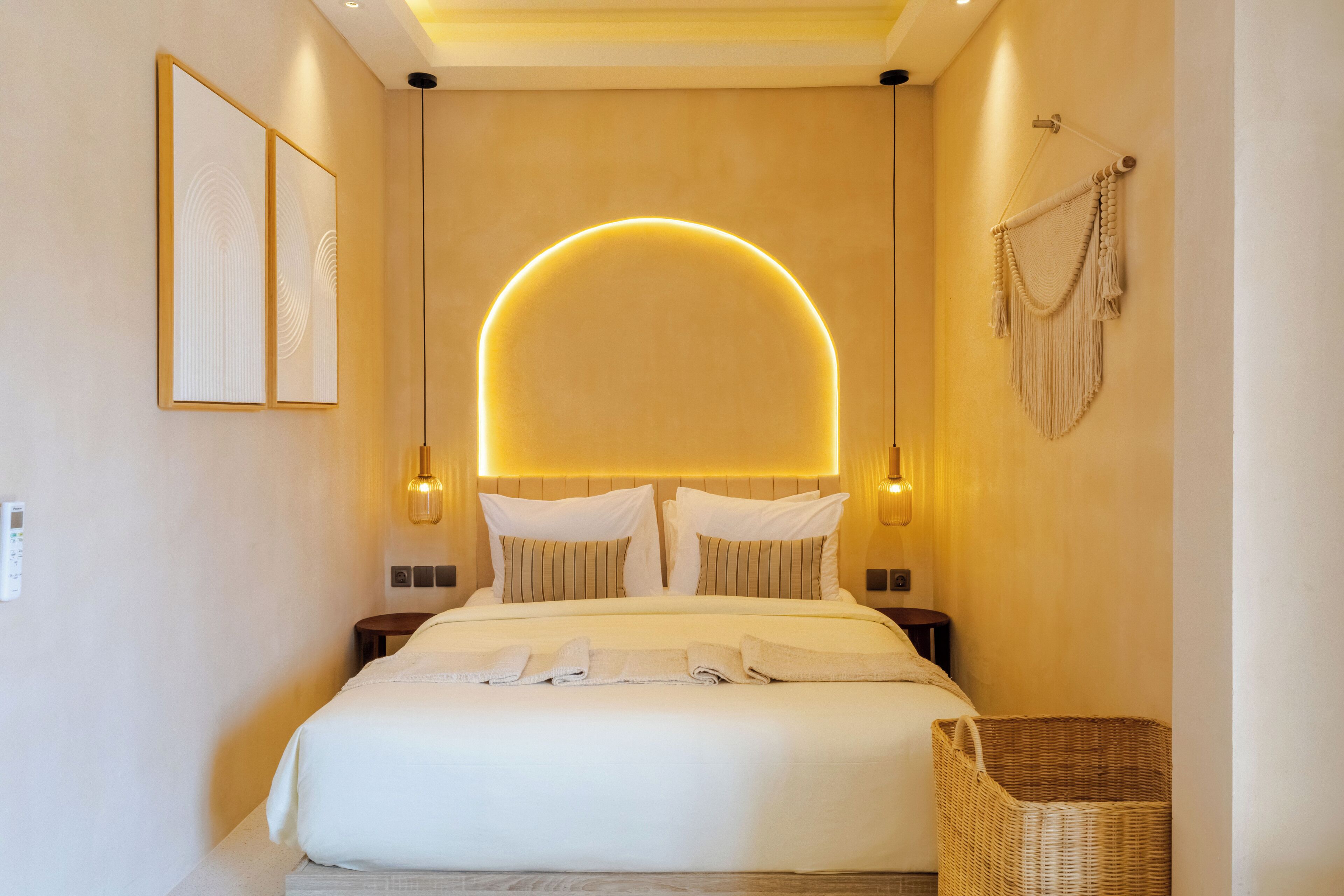A modern hotel room with a large bed, two bedside tables, a wall-mounted lamp, and a decorative macrame wall hanging.