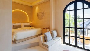 A modern hotel room with a large bed, a sofa, and a view of the outdoors through a large window. - Villa San Miguel by Pertama Stay (Seminyak)