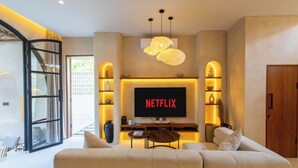 A modern living room with a large flat-screen TV displaying 'NETFLIX', a sofa, a coffee table, and a TV stand with shelves. - Villa San Miguel by Pertama Stay (Seminyak)