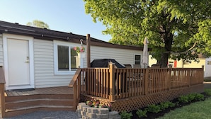 A wooden deck with a railing, a barbecue grill, and a tree providing shade. - Cozy Charming house in Oswego NY, with WiFi and AC (Oswego)
