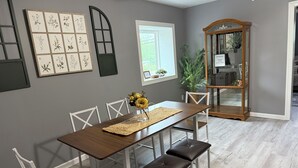 A dining area with a wooden table, white chairs, a woven placemat, and a floral centerpiece. - Cozy Charming house in Oswego NY, with WiFi and AC (Oswego)