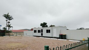 A small, single-story building with a red roof, surrounded by a gravel area and a green metal fence. - Clean and convenient cabin Centrally located in Atherton township. (Atherton)