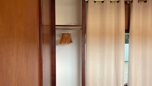 A bedroom with a wooden wardrobe, a bed with a floral bedspread, and a window with beige curtains. - Clean and convenient cabin Centrally located in Atherton township. (Atherton)