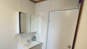 A small, clean bathroom with a white sink, mirror, and cabinet. There is a wooden floor and a white trash can. - Clean and convenient cabin Centrally located in Atherton township. (Atherton)