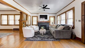 A spacious living room with hardwood flooring, a fireplace, a ceiling fan, and large windows with blinds. - Oasis in Oklahoma City (Oklahoma City)