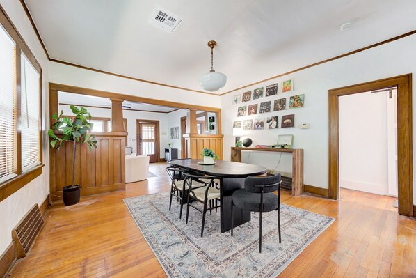 A spacious dining area with a round table, chairs, and a large rug. There is a potted plant and a mirror on the wall.