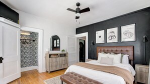 A bedroom with a large bed, a ceiling fan, a wooden bench, and a wall with framed pictures. - Oasis in Oklahoma City (Oklahoma City)