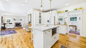 Una cocina amplia con armarios blancos, una isla central e iluminación colgante.
