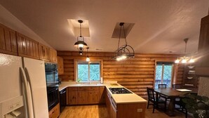 A log cabin interior with a kitchen, dining area, and a large window.