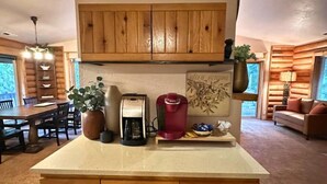 A wooden cabin interior with a kitchen area, dining table, and a living room with a sofa.