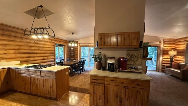 A log cabin interior with a kitchen island, dining area, and a living room with a fireplace.
