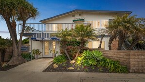 A two-story building with a balcony, palm trees, and a sign for Sunset Shores. - 1 Bed Beach Condo #131 1 Bedroom Condo by Sunset Shores Condominiums (Carpinteria)