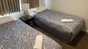 A hotel room with two single beds, a small table with a lamp, and a window with curtains.