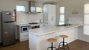 A modern kitchen with white cabinetry, a stainless steel refrigerator, a microwave, and a gas stove. There are two stools at the island and a window above the sink.