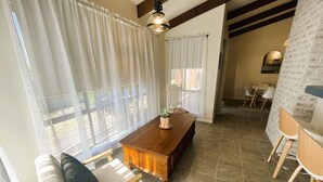 Una habitación amplia con una mesa de madera para comer, un sofá y un ventanal con cortinas de gasa.