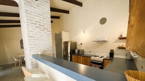 Una cocina moderna con encimera azul, taburetes de bar blancos, pared de ladrillo decorativa y un cuenco de madera sobre la encimera.