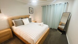 Un dormitorio con una cama de madera, una mesita de noche, un espejo y cortinas claras.