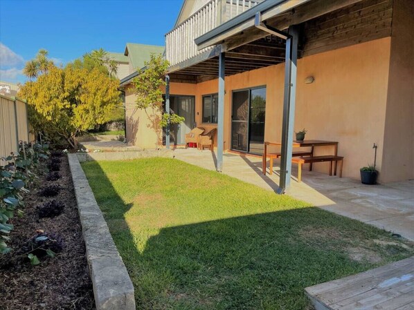 A backyard with a wooden deck, a small lawn, and a patio area with outdoor furniture.