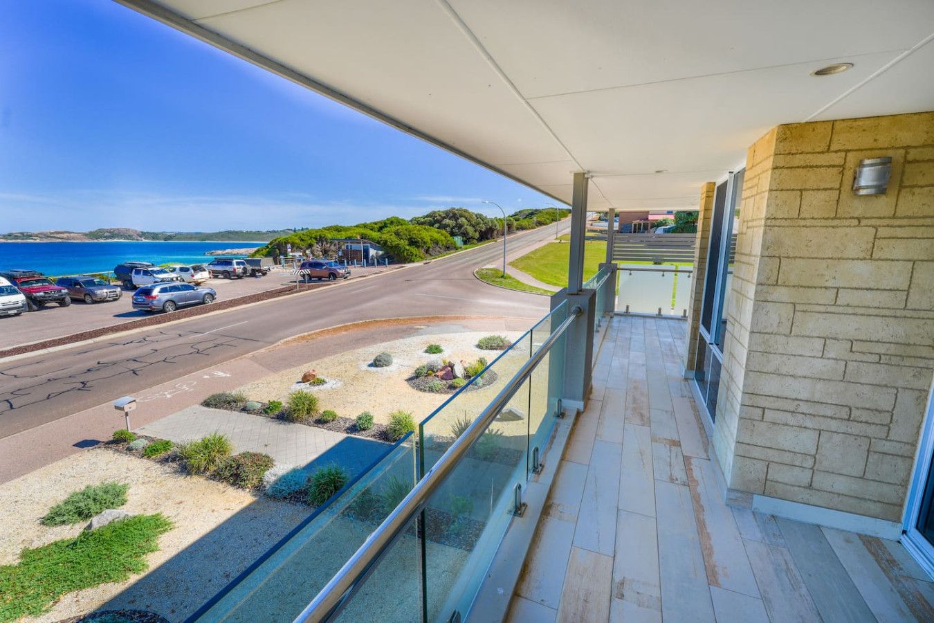 A balcony with a view of a parking lot and a road leading to a beach.