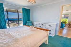 Een slaapkamer met een groot bed, uitzicht op zee en een balkon met een stoel.