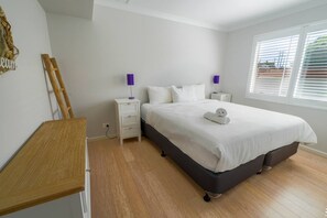 Un dormitorio con cama, mesitas de noche, un escritorio de madera y una ventana con persianas.