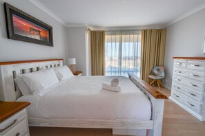 Een hotelkamer met een groot bed, een nachtkastje, een lamp, een stoel, een dressoir en een raam met gordijnen.