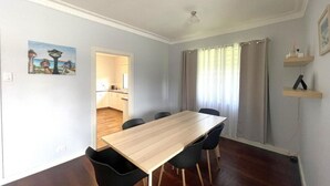 A dining area with a wooden table and black chairs, a kitchen in the background, and a painting on the wall. - Dempster House Esperance (Esperance)