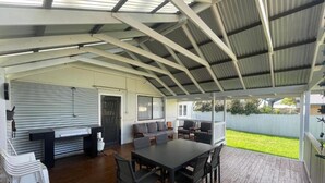 An enclosed patio with a wooden deck, a dining table with chairs, a sofa, and a grill area. - Dempster House Esperance (Esperance)