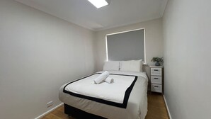 Una habitación de hotel moderna con una cama bien hecha, una mesita de noche con cajones y una pequeña planta en maceta.