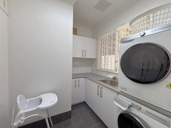 A compact laundry room with a washing machine, a drying rack, and a small white chair. - Stewart`s House Esperance (Esperance)