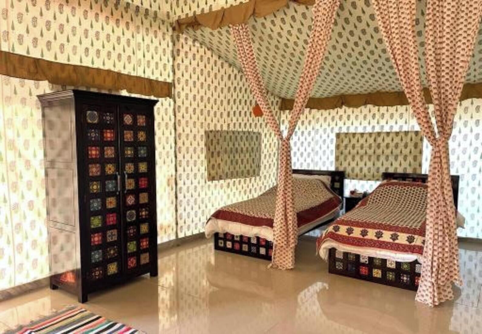 A room with two beds, a wardrobe, and patterned wallpaper.