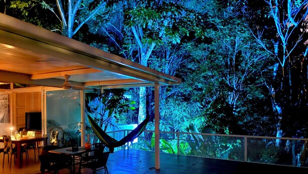 A poolside area with a hammock, dining table, chairs, and a view of a forested area at night. - Beautiful Villa Lucia, Gated Tropical Retreat, Private Deck with Pool, Ojochal (Provincia de Puntarenas)