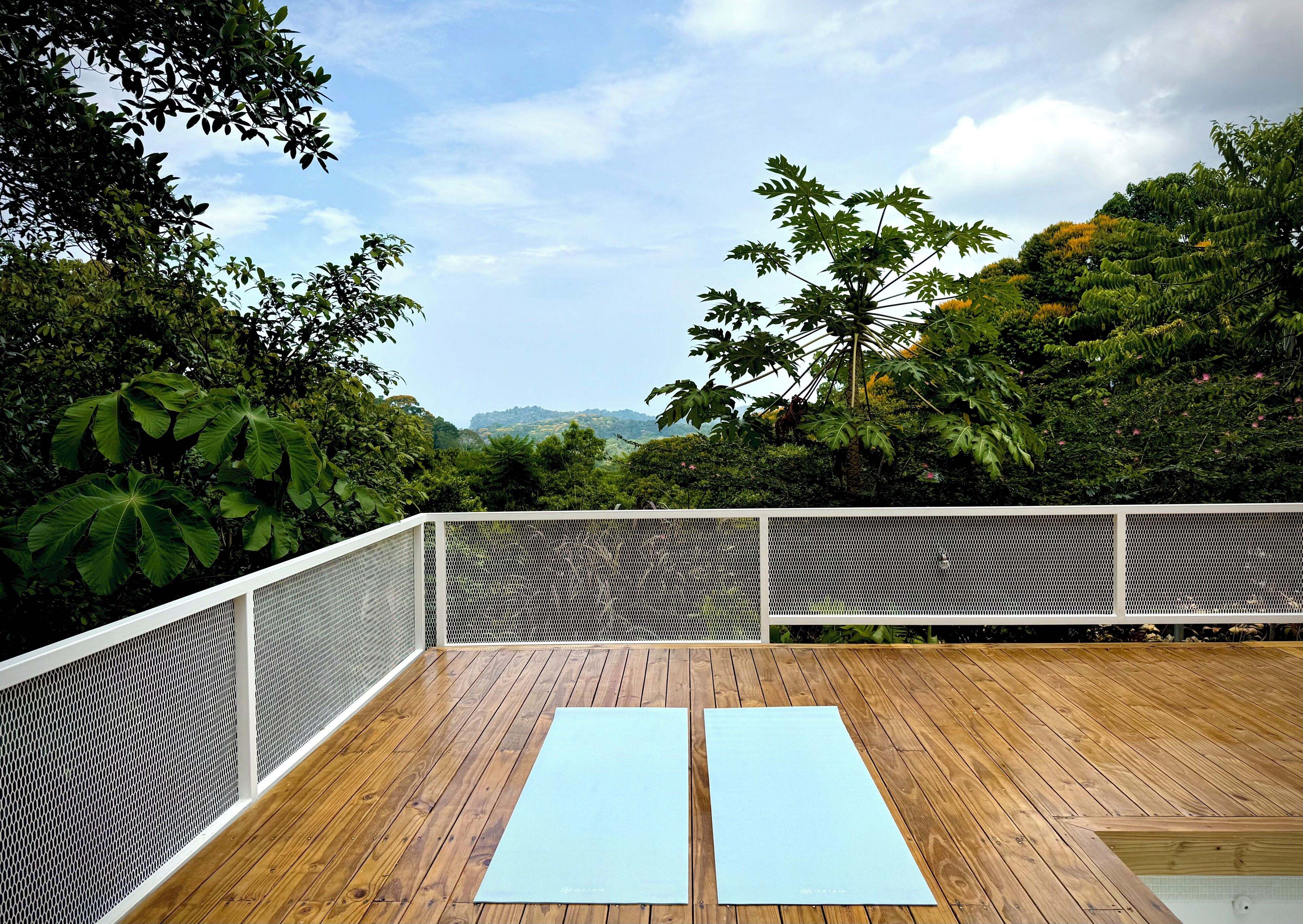 Une terrasse en bois avec deux tapis de yoga, entourée d’une rambarde en treillis blanc et d’une végétation luxuriante.