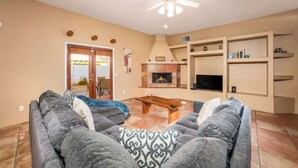 A living room with two grey sofas, a wooden coffee table, a fireplace, and a ceiling fan. - Private Pool Home with Patio | La Quinta Cove (La Quinta)