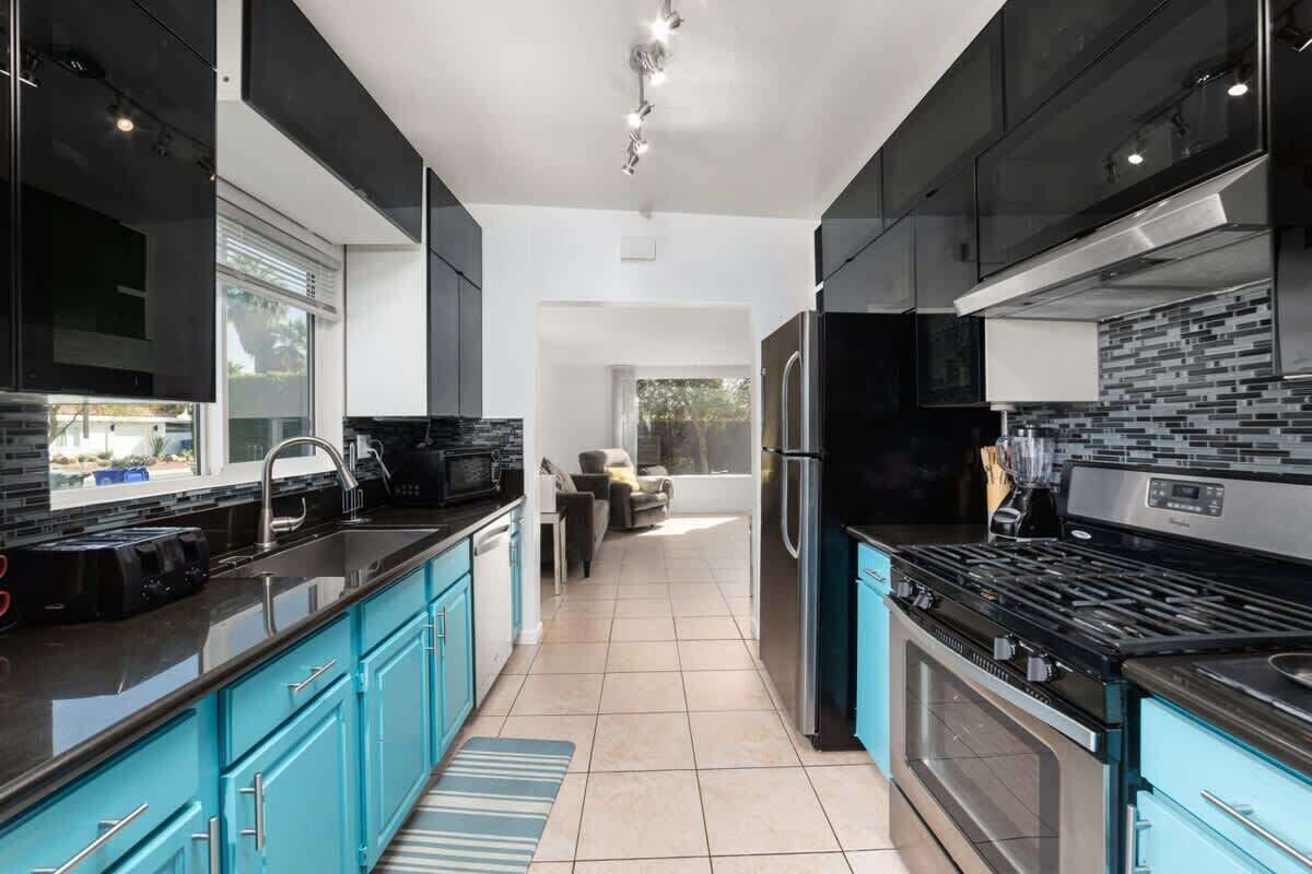 A modern kitchen with black and teal cabinetry, a black stove, and a stainless steel refrigerator.