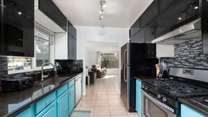 A modern kitchen with black and teal cabinetry, a black stove, and a stainless steel refrigerator. - Palm Springs Mid-Century | Mtn Views, Pool & Spa (Palm Springs)