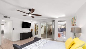 A modern bedroom with a bed, a ceiling fan, a TV, and a sliding glass door leading to a balcony. - Palm Springs Mid-Century | Mtn Views, Pool & Spa (Palm Springs)