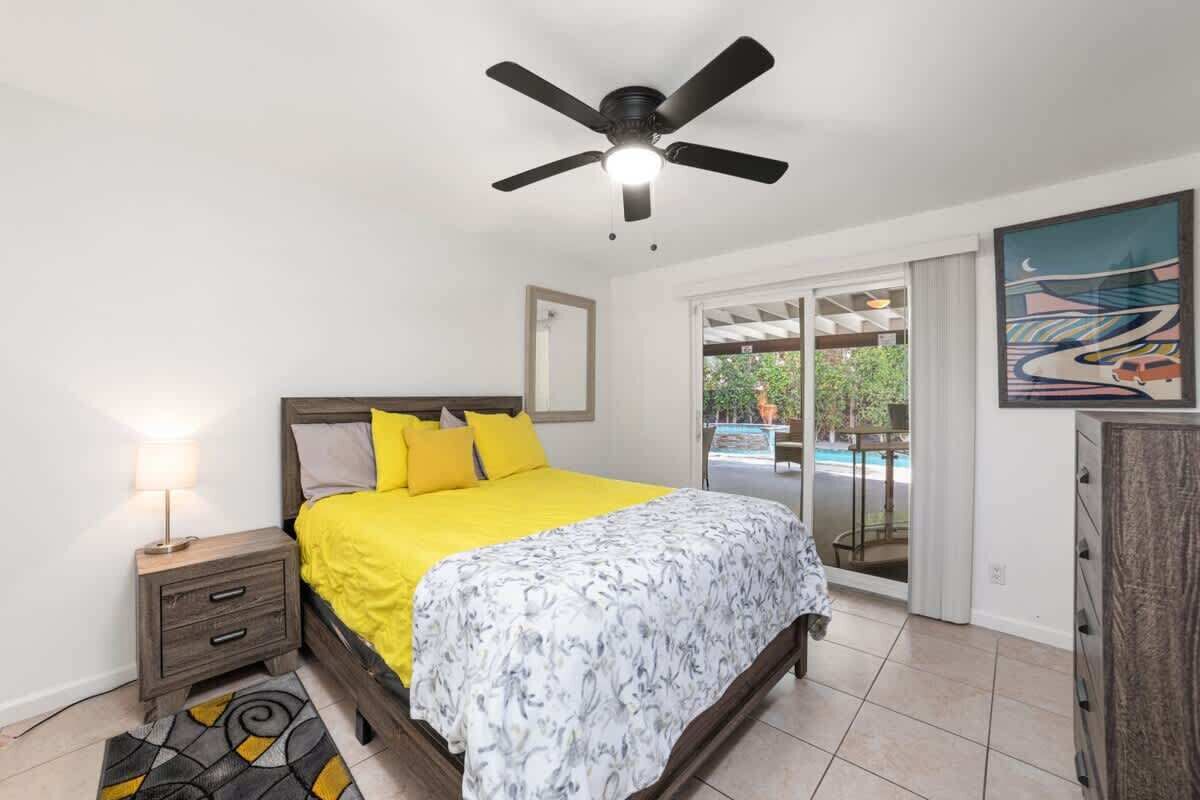 A bedroom with a bed, a nightstand, a ceiling fan, a window, and a door leading to a balcony.