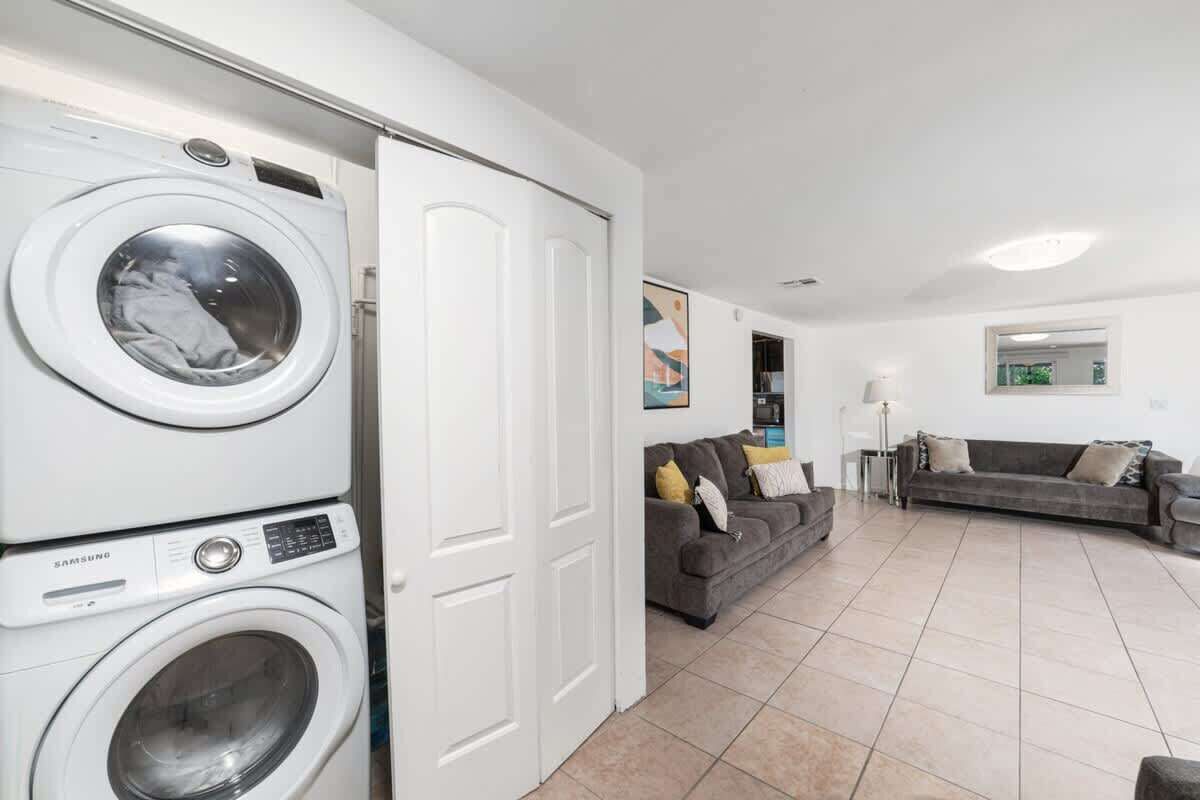 A laundry area with stacked washing machines and a grey sofa in a living room with tiled flooring.