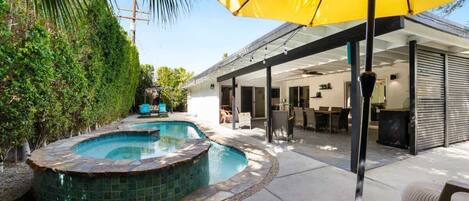 A backyard with a swimming pool, outdoor furniture, and a covered patio area.