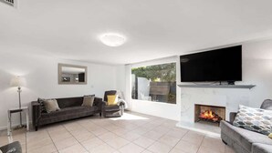 A modern living room with a fireplace, a large flat-screen TV, and a comfortable seating area. - Palm Springs Mid-Century | Mtn Views, Pool & Spa (Palm Springs)