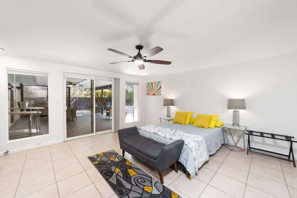 A bedroom with a bed, bedside lamps, a ceiling fan, a bench, and a view through a sliding door to an outdoor area.